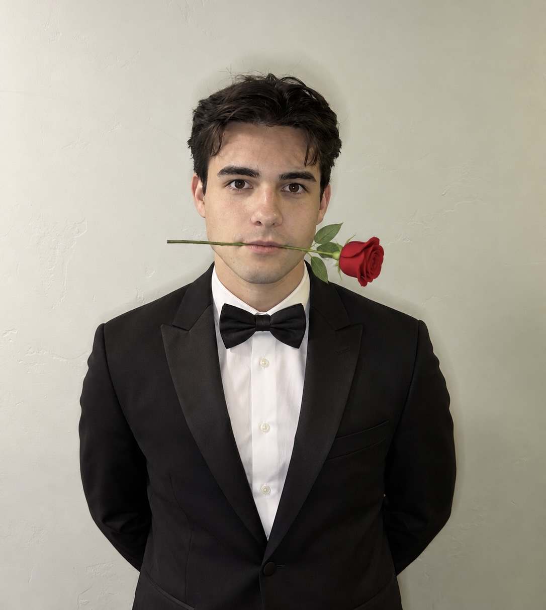 Luke Ferre in a tuxedo holding a rose in his teeth